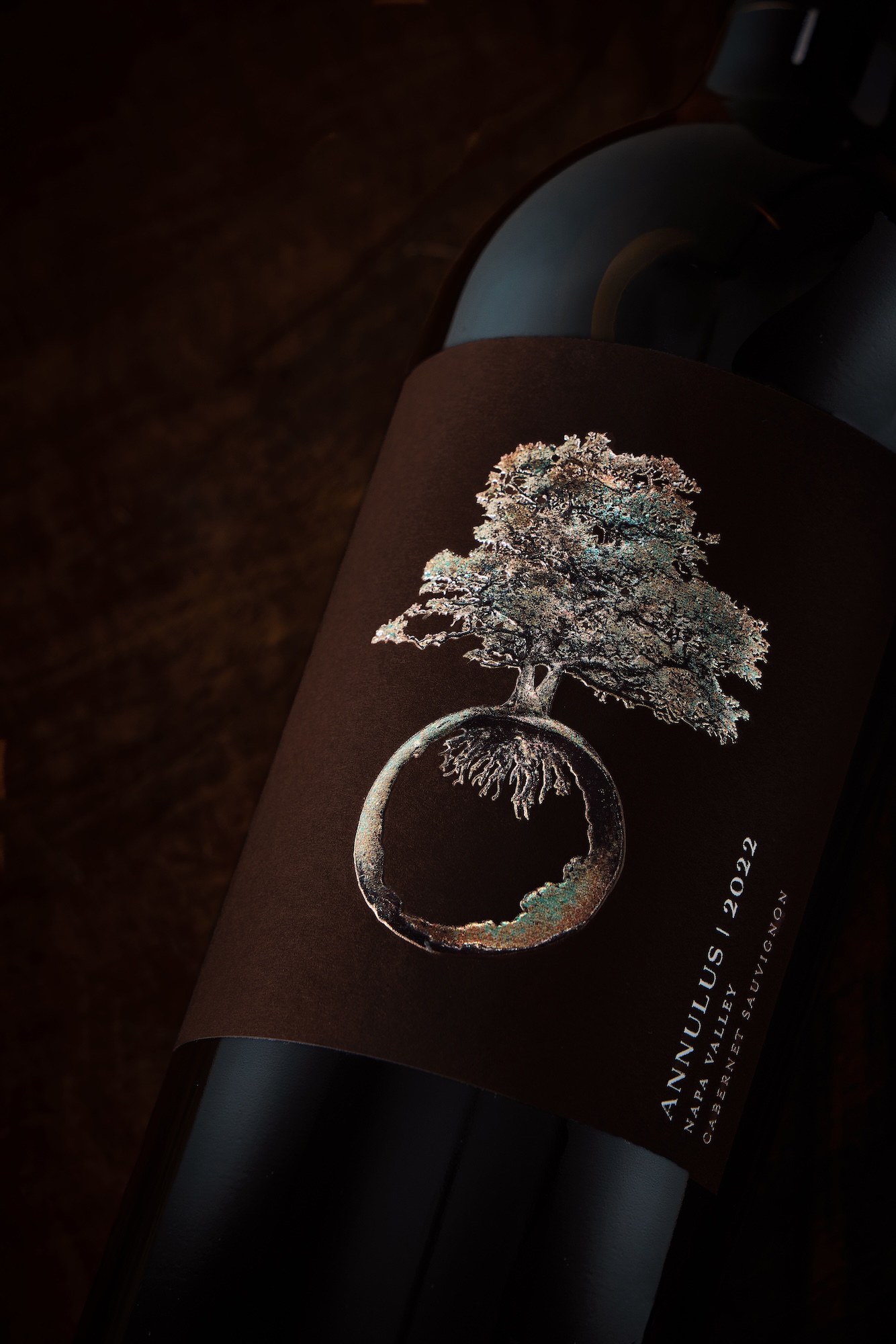 vertical bottle on dark background with turquoise and gold tree icon on label